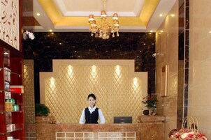 Zona de recepción con recepcionista, candelabro, pared de mármol y mostrador de atención.