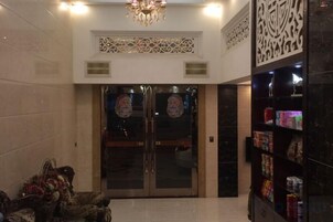 Un vestíbulo con una araña, puertas dobles con paneles de vidrio decorativo y una estantería con diversos objetos.