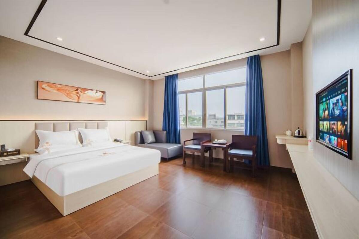 A hotel room with a bed, a desk, a chair, a TV, and a window with curtains.