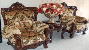 Una habitación con dos sillones de madera ornamentados, una mesita auxiliar a juego y un jarr ón de flores.