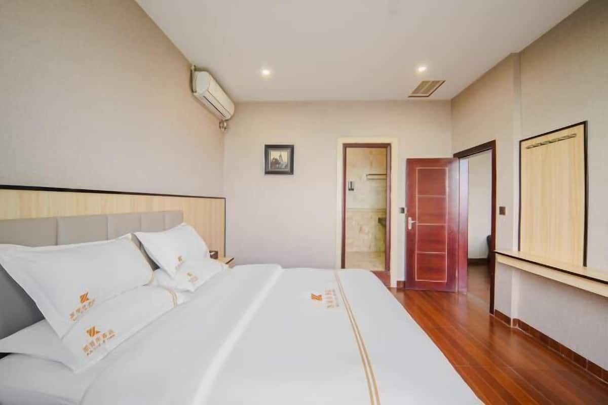 A hotel room with a bed, a wardrobe, a door, and an air conditioning unit.