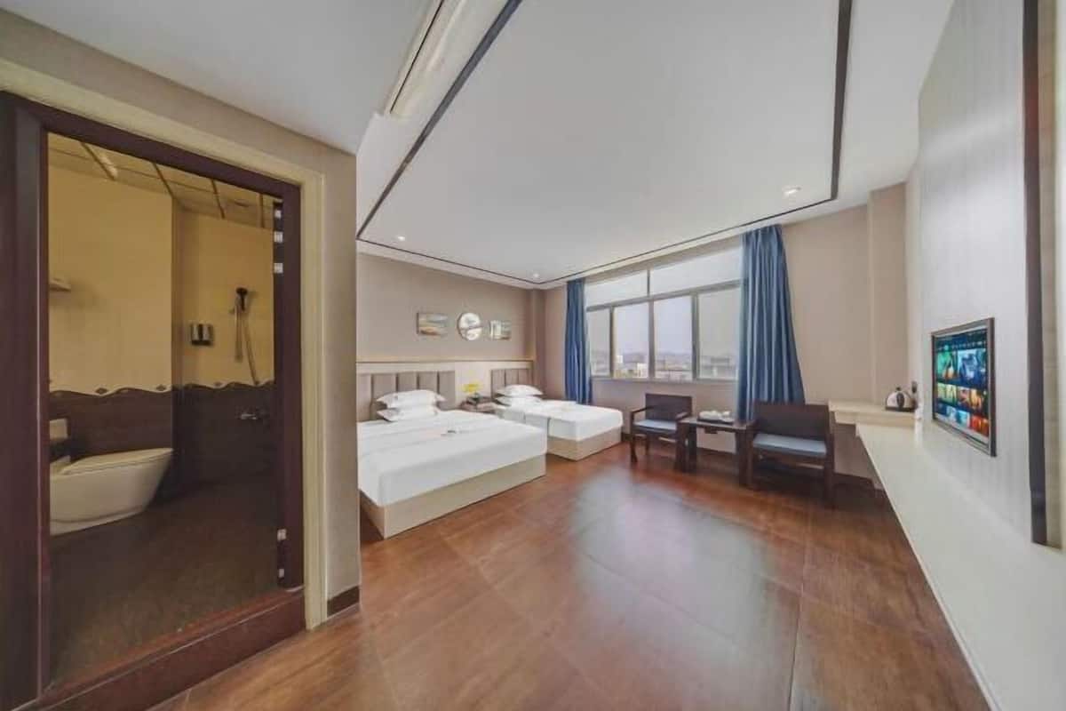 A hotel room with a large bed, a smaller bed, a desk, and a chair. There is a window with a view of the city.