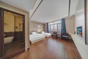 Habitación de hotel con una cama grande, una cama más pequeña, un escritorio y una silla. Hay una ventana con vistas a la ciudad.