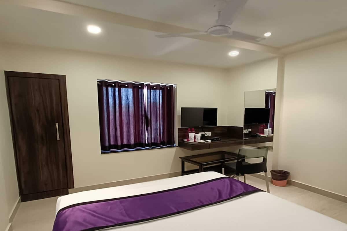 A bedroom with a bed, a desk, a chair, a wardrobe, a ceiling fan, and a window with curtains.