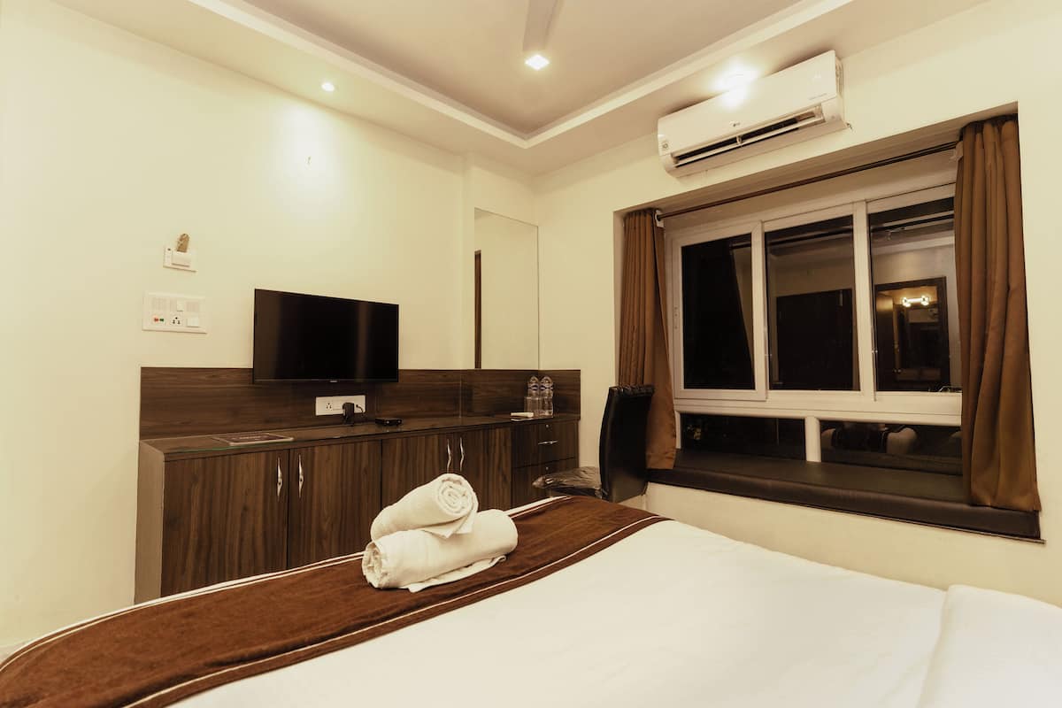 A hotel room with a bed, a TV, a wardrobe, and an air conditioning unit.