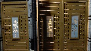 A building entrance with three large metal gates, each featuring a floral design and a vertical sign with numbers. - Hotel Sheldon Inn (Kolkata)