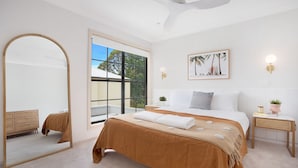 Un dormitorio con una cama grande, un espejo, una ventana con vistas a árboles y un cuadro colgado en la pared.