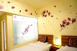 A hotel room with two beds, a large window with a view, and floral wall art.