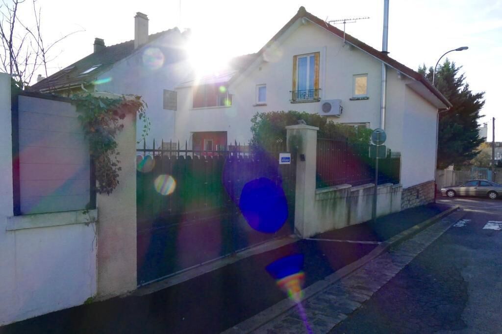 Una casa de dos pisos con fachada blanca, un balcón y una entrada protegida por una reja.
