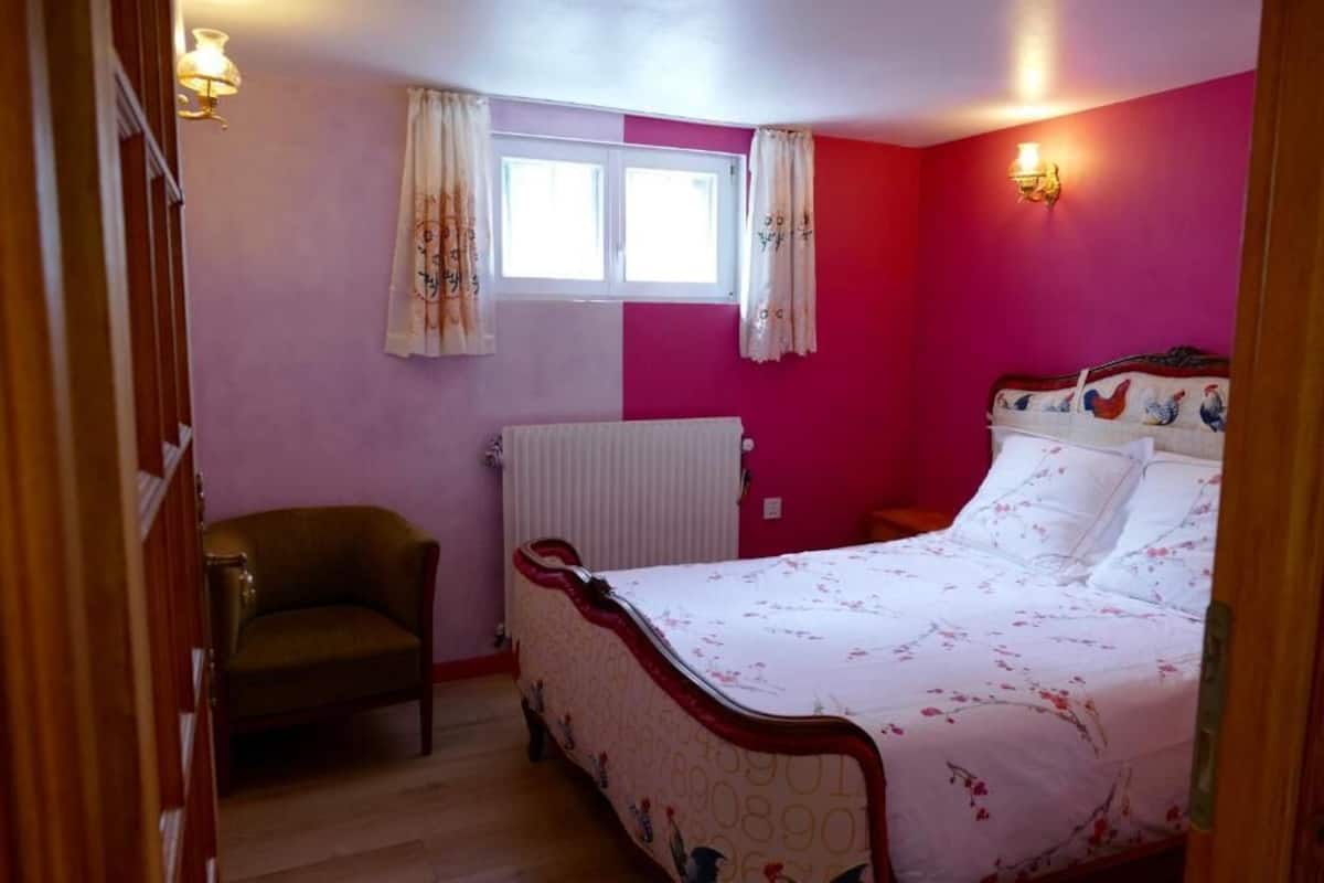 A bedroom with a bed, a radiator, a window with curtains, and a chair.