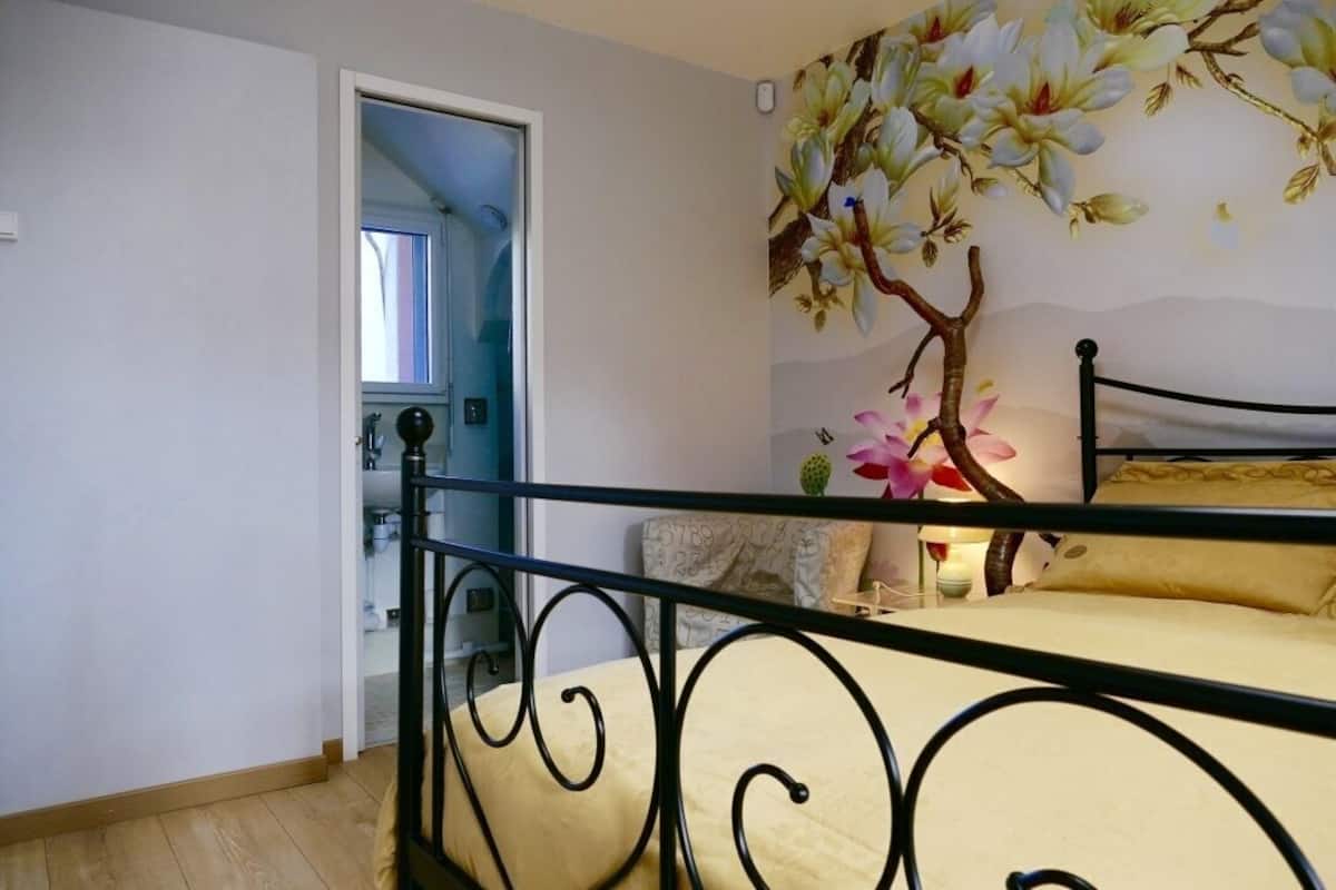 A bedroom with a bed, a door leading to another room, and a wall with a floral mural.