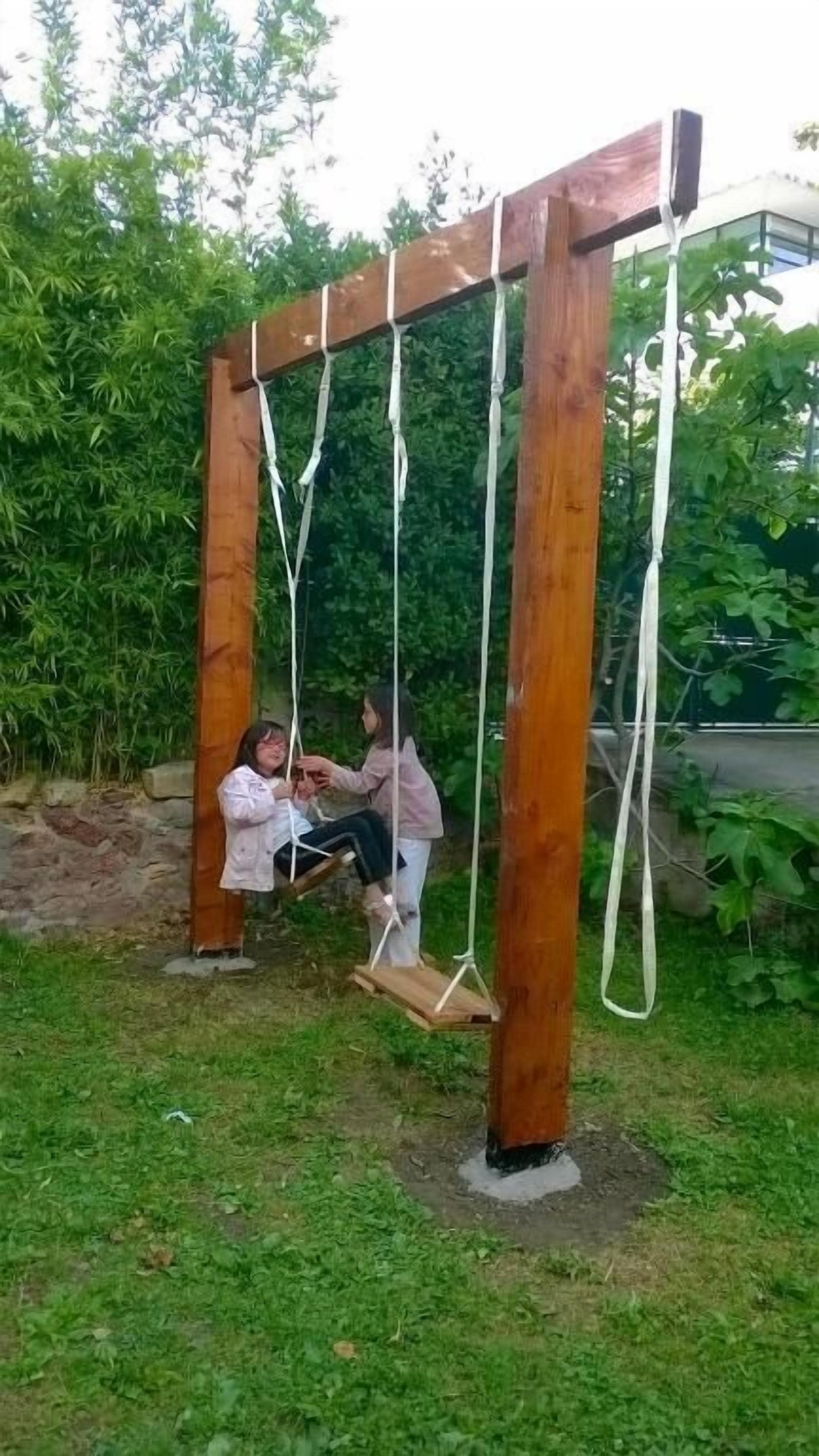 A wooden swing set in a grassy area with dense foliage in the background.