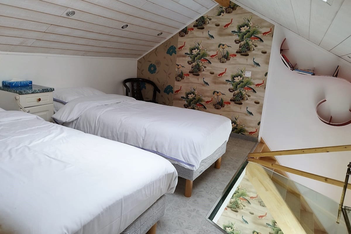 A bedroom with two beds, a wooden ceiling, a decorative wall, and a small table with books.