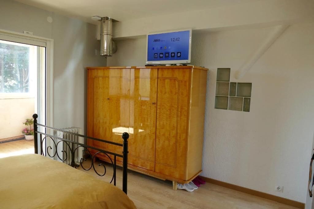 A bedroom with a bed, a wooden wardrobe, a small heater, and a window.