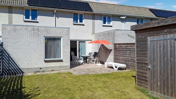 Ein Wohnhaus mit Backsteinfassade, einer kleinen Terrasse mit Gartenmöbeln und einem Holzzaun.