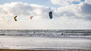 Ein Strand mit Wellen und drei Drachen am Himmel.