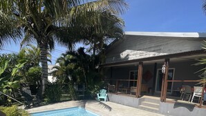 Een zwembad met betegeld zonnedek, omringd door palmbomen en een gebouw met een overdekte patio.