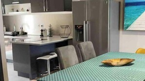 Een moderne keuken met een centraal eiland, een eethoek met een tafel en stoelen, en uitzicht op zee door een raam.