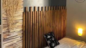 Een kamer met een houten lattenbed, een aan de muur bevestigde droomvanger, een bedlamp en een matras met beschermhoes.