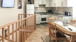 Cocina con armarios blancos, microondas, estufa y lavaplatos. Hay una mesa de comedor de madera con sillas y una planta en maceta encima.