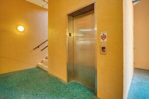 An elevator in a hallway with a tiled floor, a wall-mounted light, and a fire safety sign. - The View at Bradenton Beach Club (Bradenton Beach)