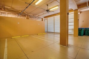 Un parking avec des planchers en béton, des piliers jaunes et des poubelles vertes.