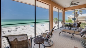 Un balcon avec vue sur la plage et l’océan, aménagé avec des chaises et une table.