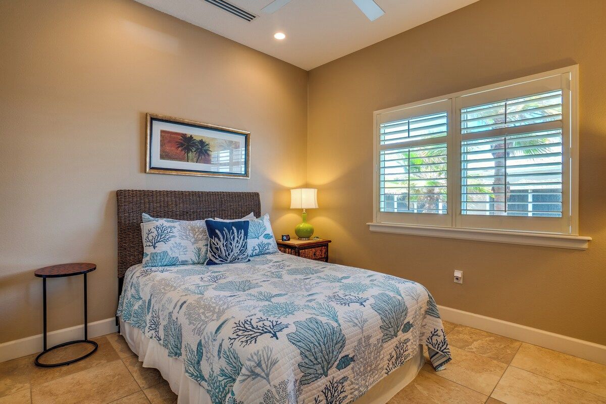 A bedroom with a bed, a nightstand, a lamp, a framed picture on the wall, and a window with blinds.