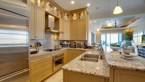 Une cuisine moderne dotée d’appareils électroménagers en acier inoxydable, de meubles de couleur beige, de plans de travail en granit et de luminaires suspendus.