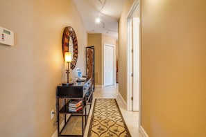 Un couloir avec un tapis à motifs, une lampe fixée au mur et une porte au fond.