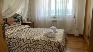 Un dormitorio con colcha estampada, cabecero de madera, mesita de noche con un globo terráqueo y cortinas translúcidas.