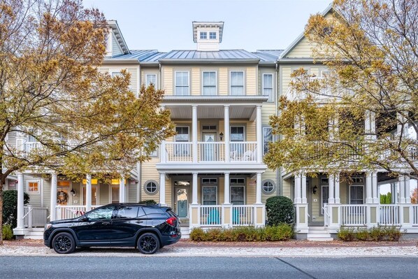 A two-story building with a balcony, a car parked in front, and trees with autumn leaves.