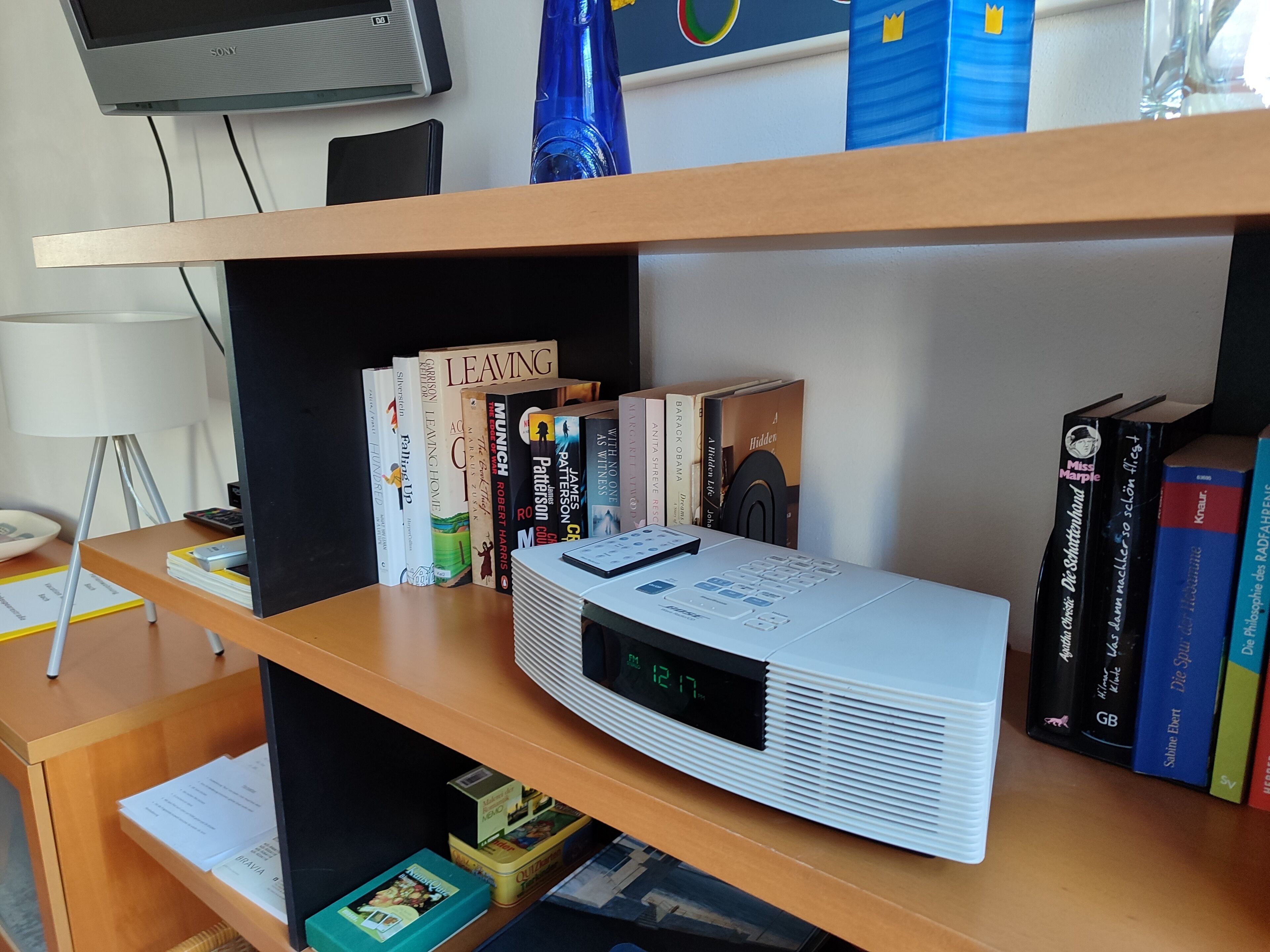 Uma estante com vários livros, um relógio digital e uma televisão.