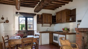 A rustic kitchen with wooden cabinets, a dining table with chairs, a refrigerator, and a window with a view of the outside.