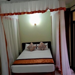 A bed with a white and orange bedspread, two patterned pillows, and a canopy with white and orange drapes.