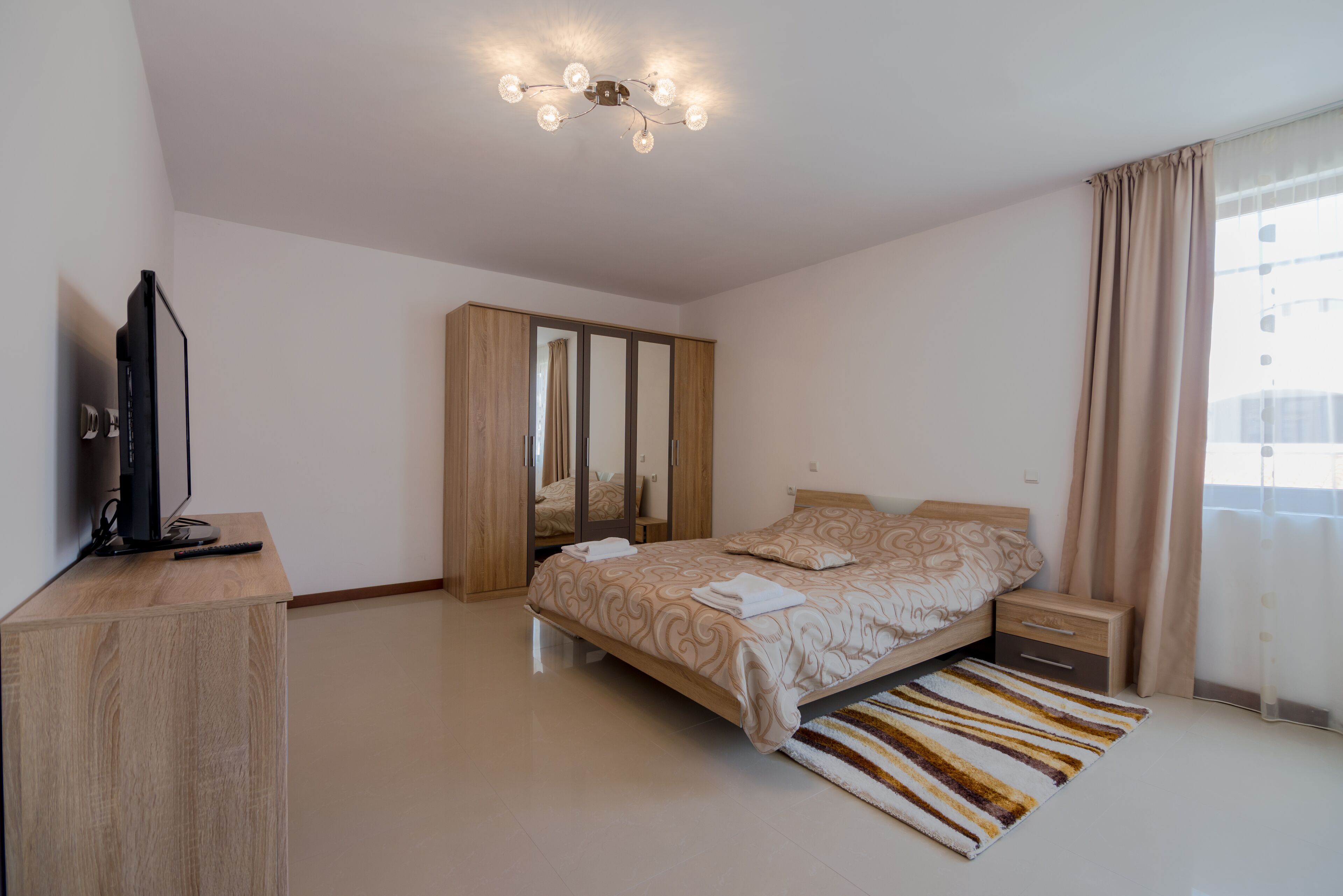 Une chambre à coucher comprenant un lit, des tables de chevet, une armoire, un téléviseur et un luminaire au plafond.