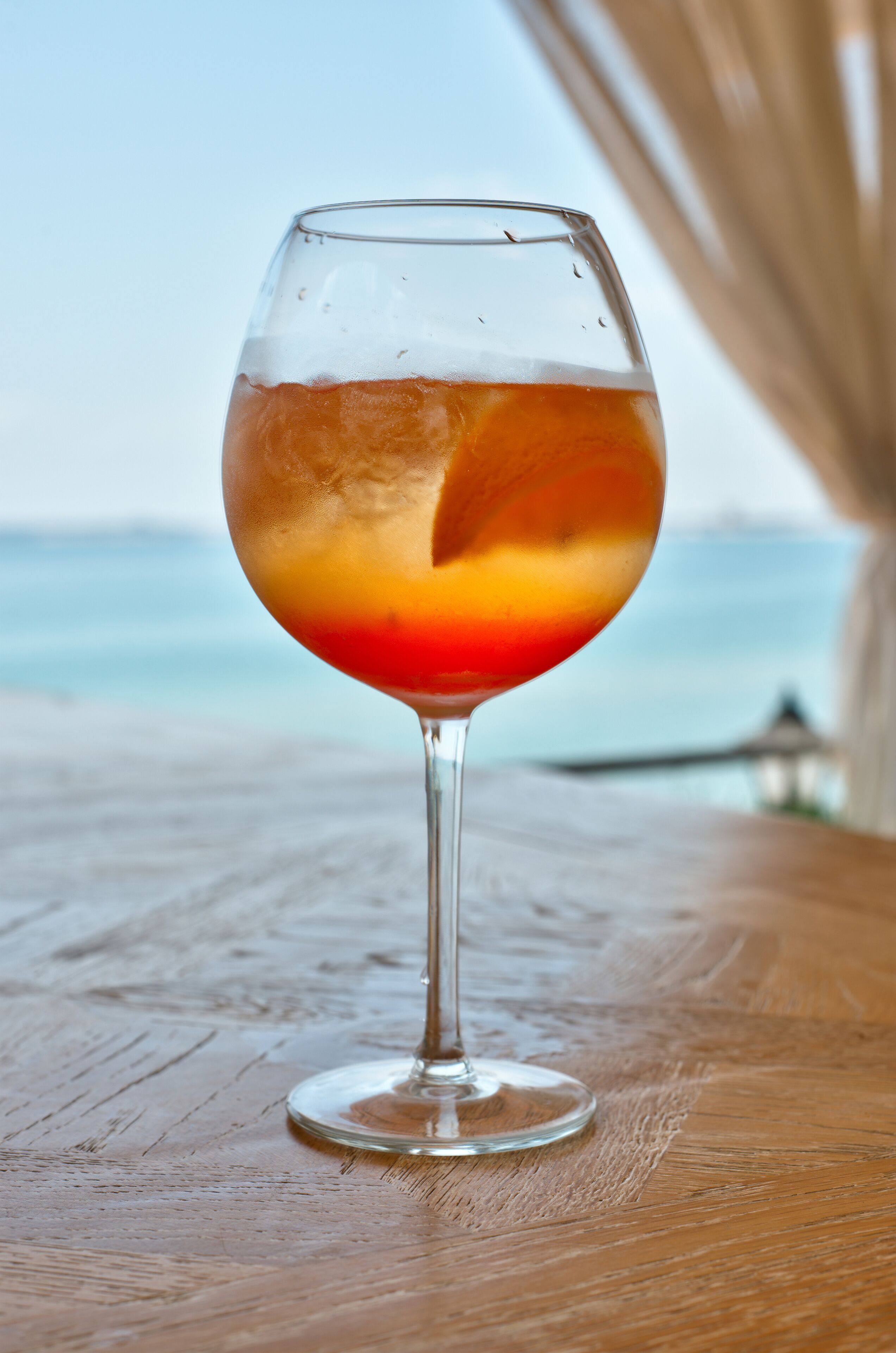 Ein Glas eisgekühltes Getränk auf einem Holztisch, im Hintergrund der Blick aufs Meer.