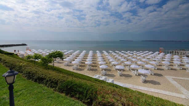 Ein Strand mit Reihen weißer Sonnenschirme und Liegestühle, ein klarer Himmel und eine ruhige See.
