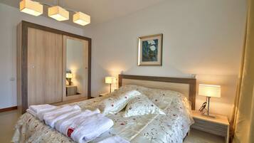 A neatly made bed with a floral duvet, a wooden wardrobe, a bedside table with a lamp, and a wall-mounted painting.
