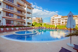 Una piscina con sillones de descanso y sombrillas, rodeada de edificios de varios pisos con balcones.