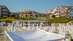 Ein Strandhotel mit mehreren weißen Gebäuden, einem überdachten Sitzbereich und zahlreichen weißen Sonnenschirmen.