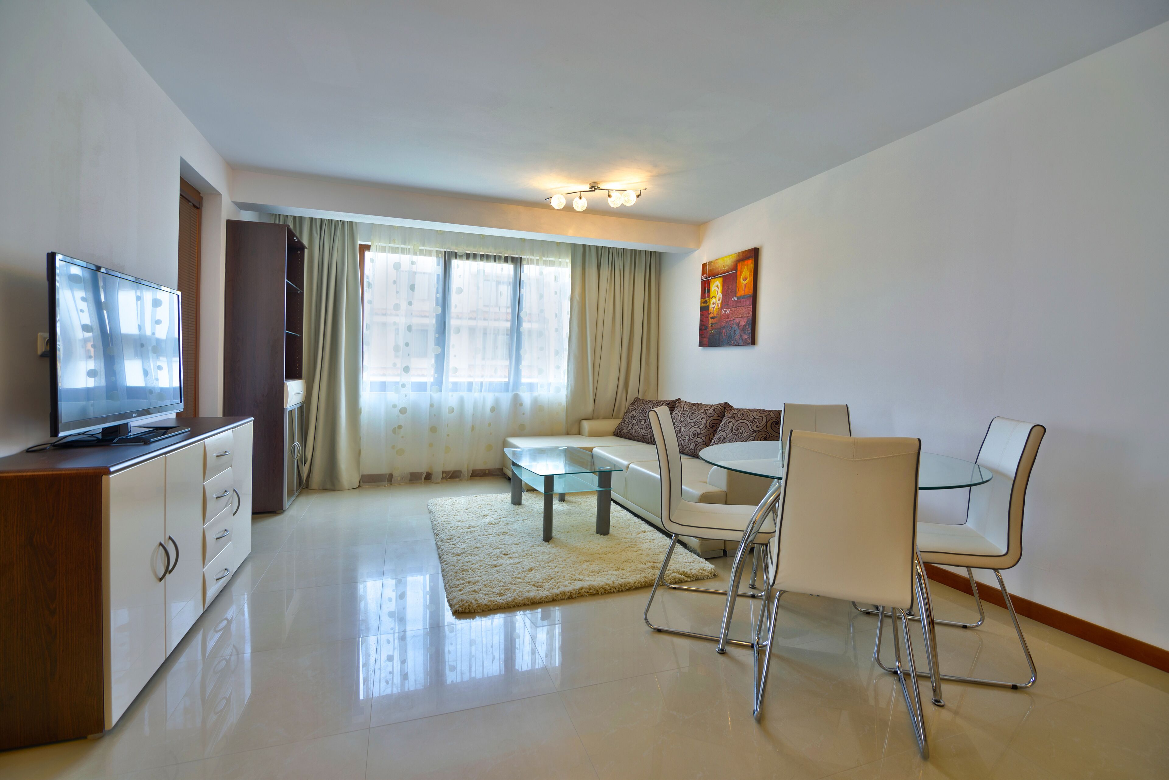 A modern living room with a flat-screen TV, a sofa, a glass dining table, and a coffee table.