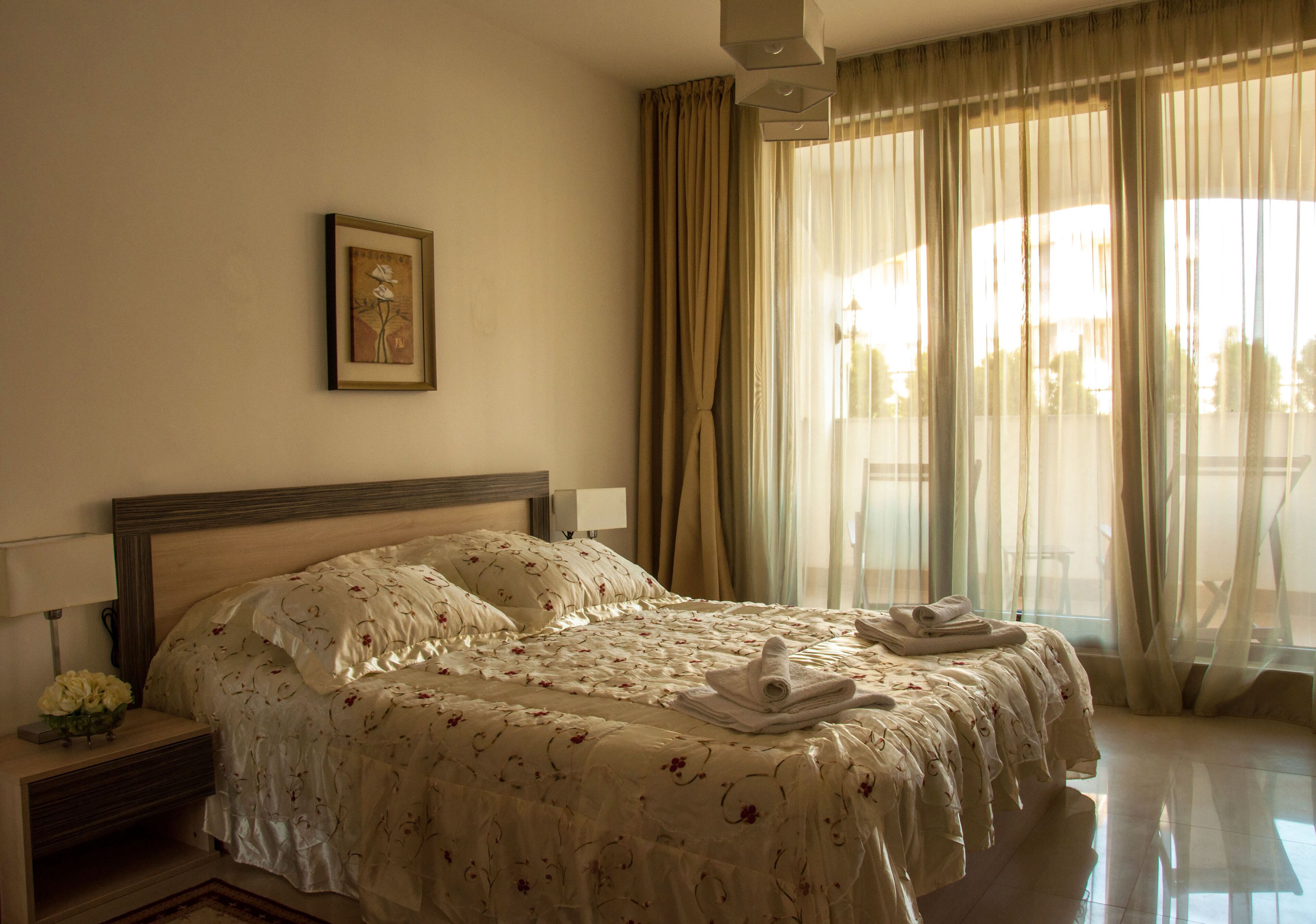 A hotel room with a large bed, a nightstand with a lamp, and a window with curtains.