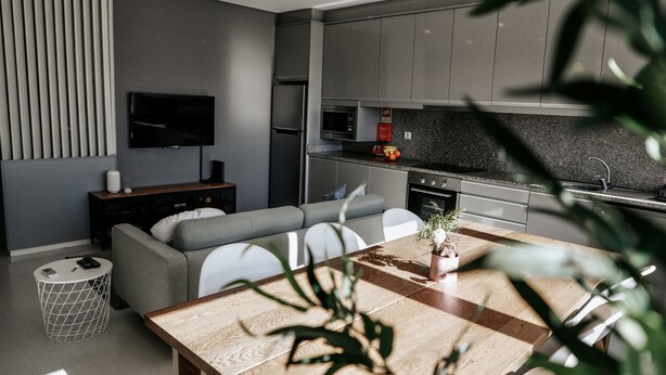 A modern kitchen with grey cabinets, a flat-screen TV, and a dining area with a wooden table and chairs.
