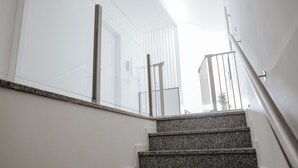 A staircase with granite steps and metal railings, leading to a bright interior space with white walls and a glass door.