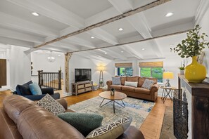 A spacious living room with a high ceiling, a television, a sofa set, a coffee table, and a large window with a view.