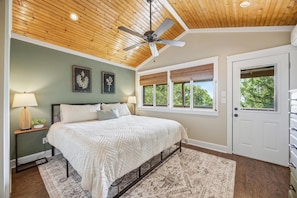 A bedroom with a bed, a ceiling fan, a window with blinds, and a door.