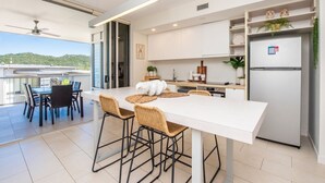 A modern kitchen with white cabinets, a built-in refrigerator, and a dining area with a white table and wicker chairs.