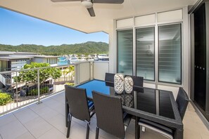 A balcony with a glass table, wicker chairs, and two decorative vases. - 1 Bright Point Apartment 1307 (Nelly Bay)
