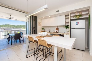A modern kitchen with white cabinets, a built-in refrigerator, and a dining area with a white table and wicker chairs. - 1 Bright Point Apartment 1307 (Nelly Bay)